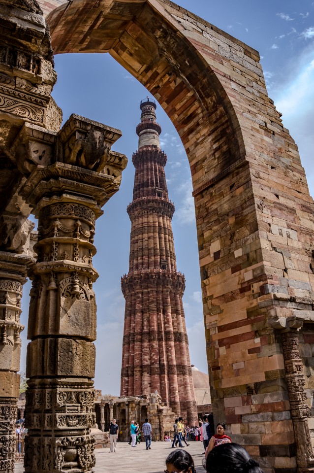 A fluted sandstone minaret framed by an ancient stone arch