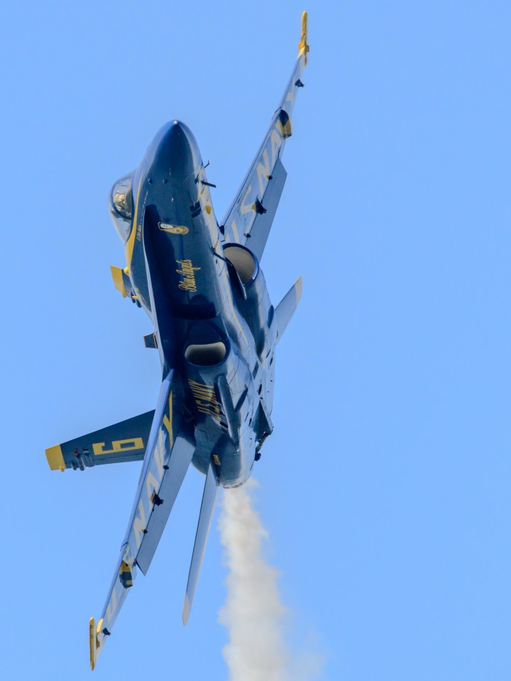 A blue-and-gold fighter jet banking against a clear sky